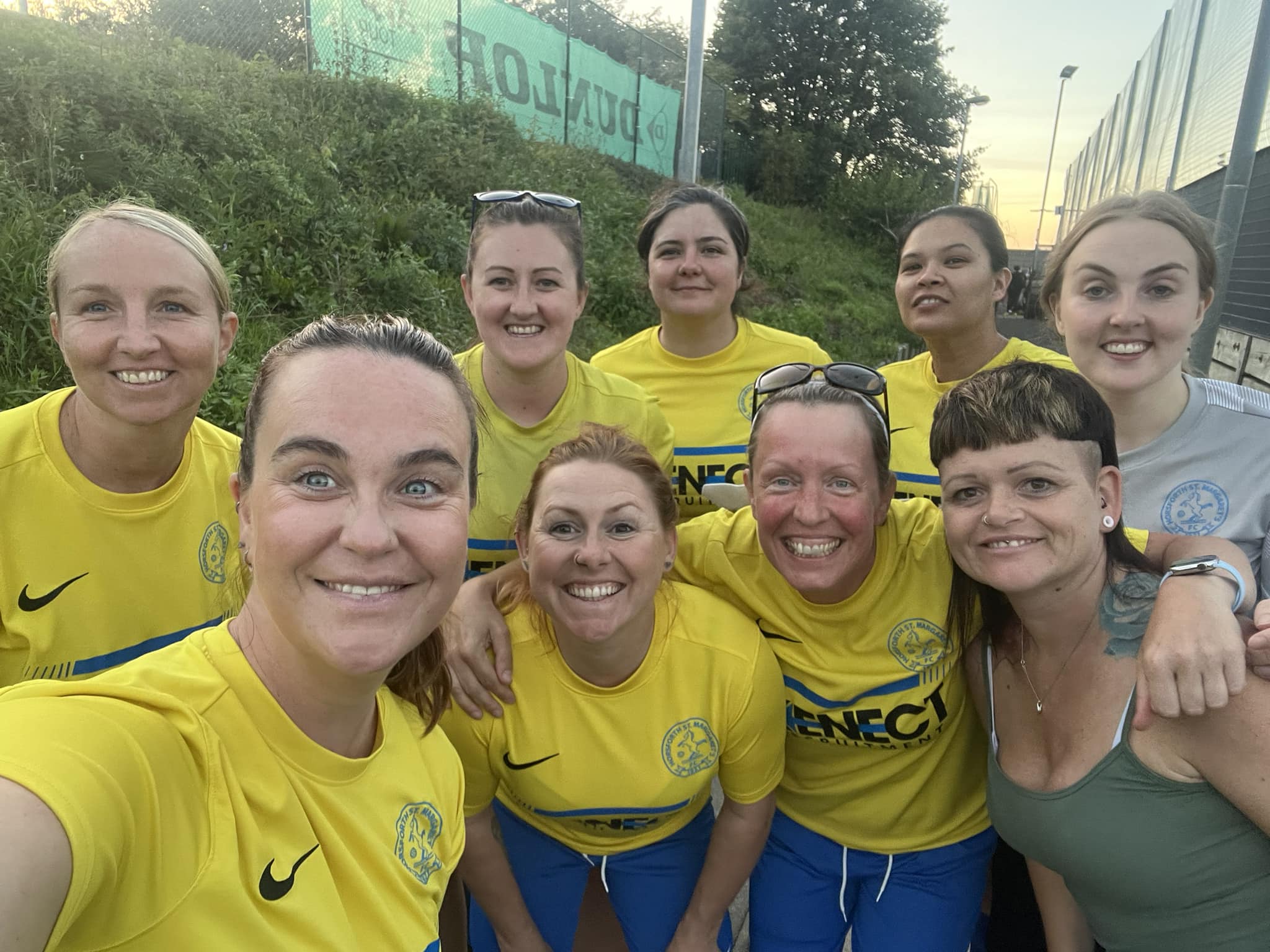 Nine adults, seven of them wearing yellow football t-shirts and the rest wearing casual clothes